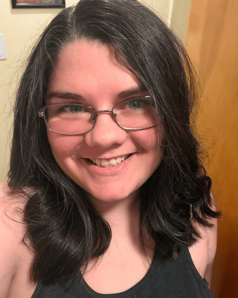 Adrienne: Close-up portrait of Adrienne smiling, wearing glasses with shoulder-length dark hair.